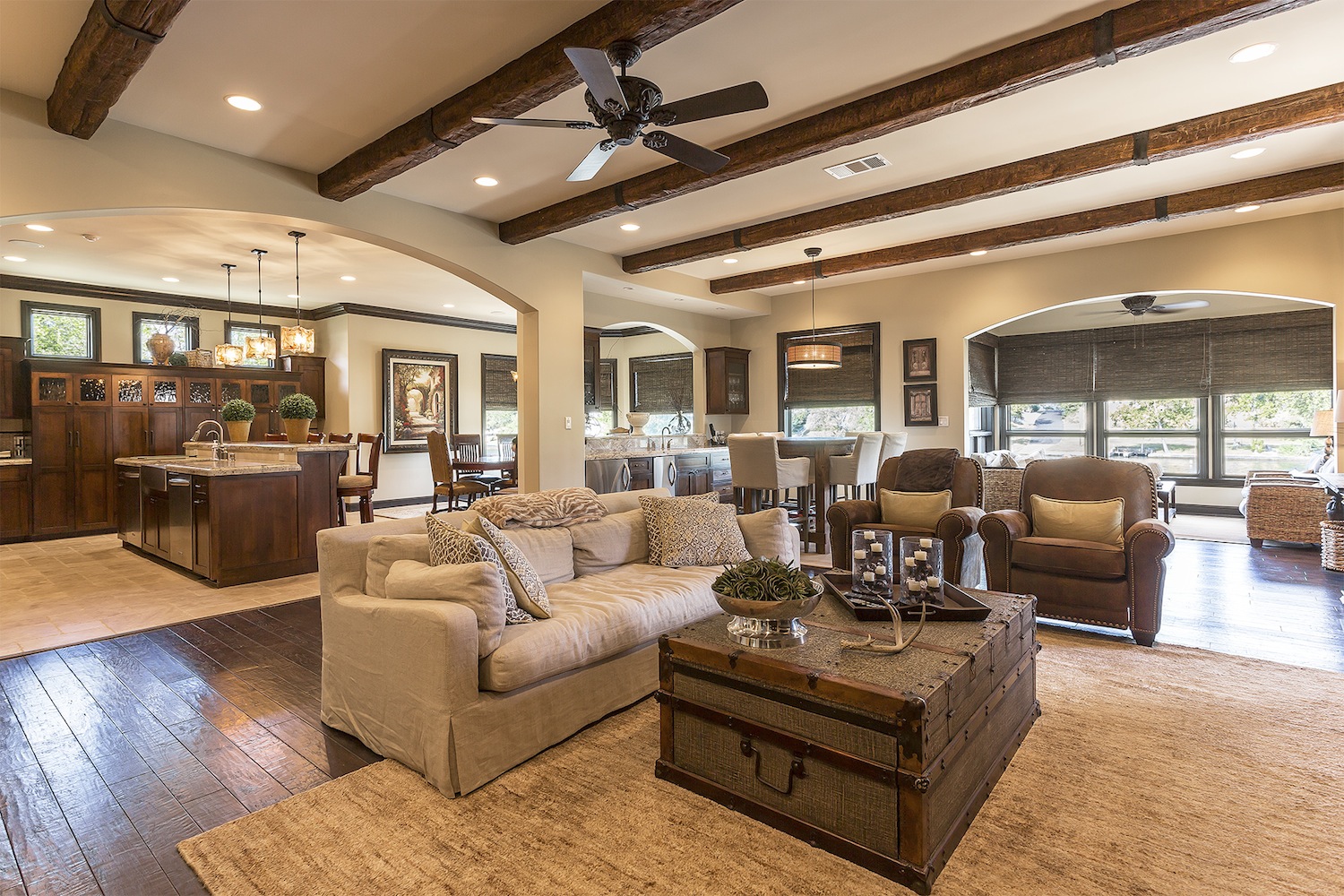 Dark faux wood beams with straps span the length of a large open-concept kitchen and great room.